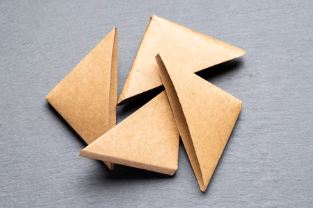 Four brown paper triangles are arranged in a circular pattern on a gray surface. The triangles are...