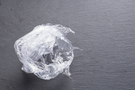 In the image you can see a crumpled and curled plastic bag on a dark surface