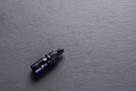 In the image you can see a glass bottle with a dark dropper lid on a gray stone background