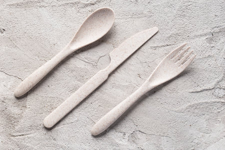 A recycled plastic spoon, knife and fork are seen on a gray cement surface