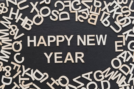 You can see in the image many wooden letters scattered on a blackboard background and a happy new...