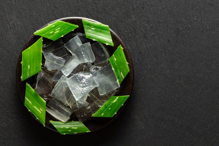 Ale Vera leaves and aloe extract are seen in a container, on a slate background, their view is from aboveの写真素材