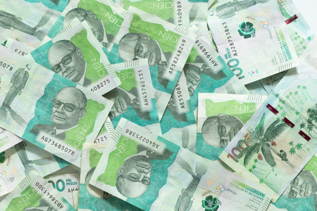 A pile of one hundred thousand Colombian peso bills is seen scattered on a flat surface, top view
