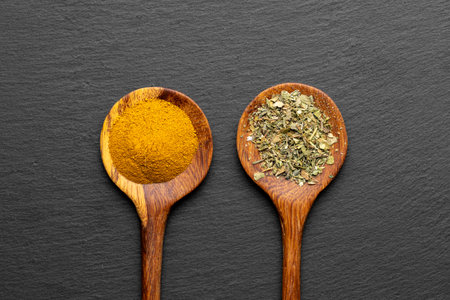 Wooden Spoons with Ground Turmeric and Dried Herbs on Slate Backgroundの写真素材