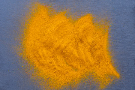 Fresh and ground turmeric root on a slate background