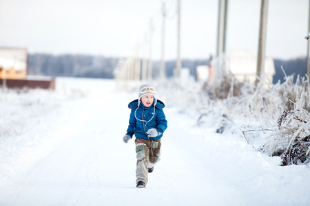 Kid boy running along the road with snow in winterの写真素材