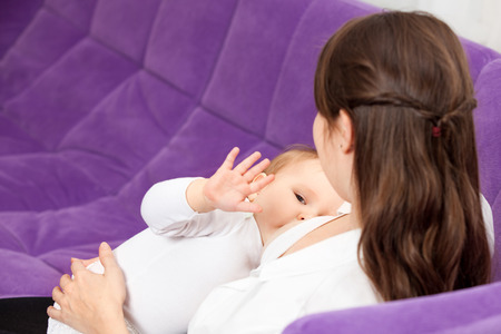 A young woman breast-feeding a baby, sitting on sofaの写真素材