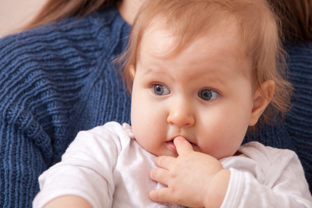 Surprised by the child in the arms of his mother keeps his finger in his mouthの写真素材