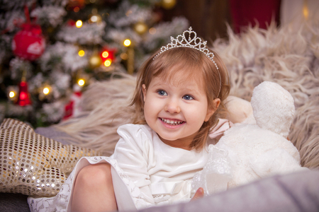 the girl smiles, a Christmas tree in the lights and a window with a garland surrounds the atmosphere of the holidayの写真素材