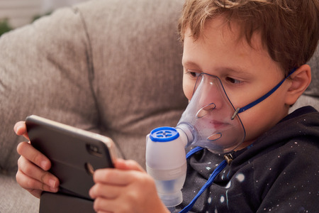 child makes inhalation nebulizer at home. on the face wearing a mask nebulizer inhaling vapor...