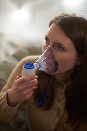 woman makes inhalation nebulizer at home. holding a mask nebulizer inhaling fumes spray the...