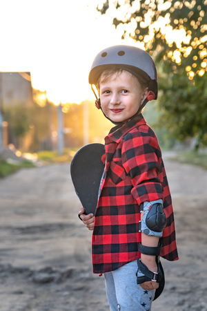 happy little boy standing on the road holding a skate with his hands. the child defended himself, he put on hand safety gloves elbows and knees wearing protective shields. on the head wearing a helmetの写真素材