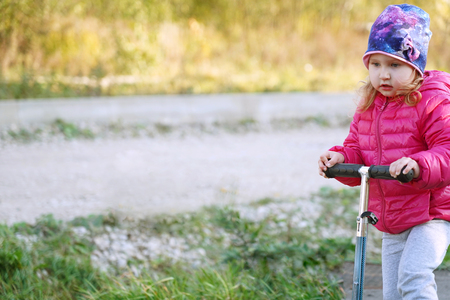 girl holding the handle of the scooter. the first experience of riding a scooter. cool weather baby is warmly dressed. learning to drive on their own. a lot of space in front of the child for textの写真素材