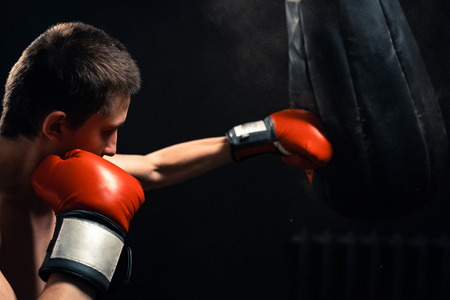 Boy hitting the punching bag on dark backgroundの写真素材