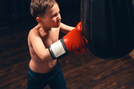 Boy hitting the punching bag on dark background. the aggression on sports trainingの写真素材