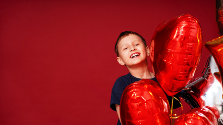 Laughting little boy, various color heart, star balloons for valentines day or birthday on red background with free text spaceの写真素材
