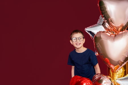 Laughting little boy in glasses, different color heart, star balloons for valentines day or birthday on red background with free text spaceの写真素材