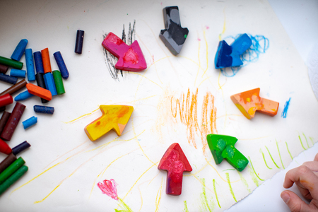 made homemade wax pencils from the wreckage of old crayons by melting them in the oven at high temperature in silicone form. crayons in the form of arrows lie on paper, hand childの写真素材