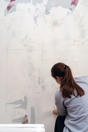 woman tears off Wallpaper, removing Wallpaper from the wall with a spatula, the process of updating the wall room repair. with free text spaceの写真素材