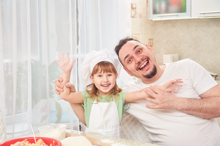 father preparing food with my daughter. the man is smiling happily together with her daughter held out her arms. positive family in a bright kitchen. fatherly care and love for cooking. girl laughsの写真素材