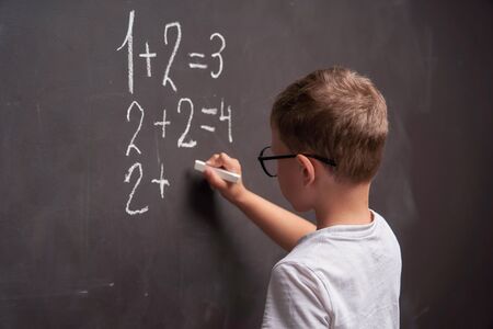 Primary education. Rear view of a schoolboy solves a mathematical example on a blackboard in a math class.の写真素材