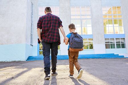 Back to school. Happy father and son go to elementary school. Parent taking child to primary school. Pupil go study with backpack. Beginning of lessons. First day of fall.の写真素材