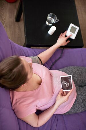 a woman measures blood pressure with an electronic pressure gauge, headache during pregnancy, poor...