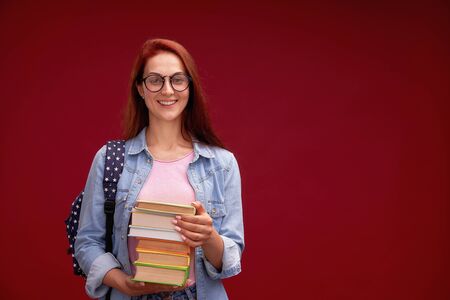 portrait of a beautiful girl student with a backpack and a stack of books in his hands is smiling at...