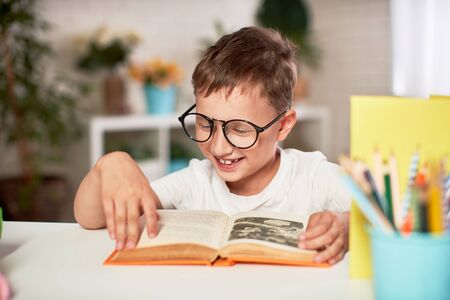 joyful little boy sitting at the table with pencils and textbooks. Happy child pupil doing homework at the table.handsome boy reading a book, home schooling. positive attitude to studyの写真素材