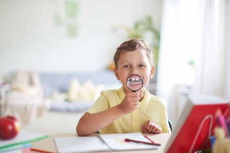 a boy with a magnifying glass in his hands smiles showing his enlarged teeth. funny portrait of a...
