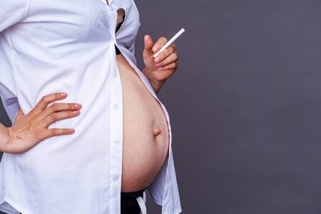 Smoking pregnancy. pregnancy and smoking cigarettes. Harm to the child's health . Premature birth. Close up pregnant woman quits smoking.On gray background. Copy spaceの写真素材