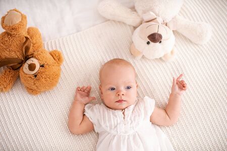 Cute little girl with blue eyes 4 months old lies on bed with Teddy bears and looks away. small...