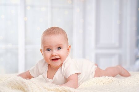 Cute baby is lying on the bed on a white blanket and smiling. a small curious child of 4 months,...