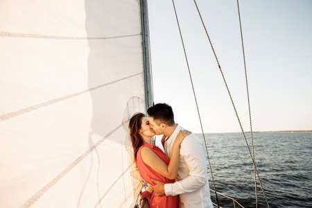 Young loving couple hug and kiss on a sailing white yacht in the sea.