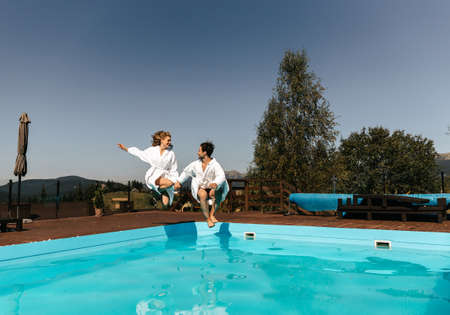 Drive young couple together by hand jumping into the pool. High quality photo