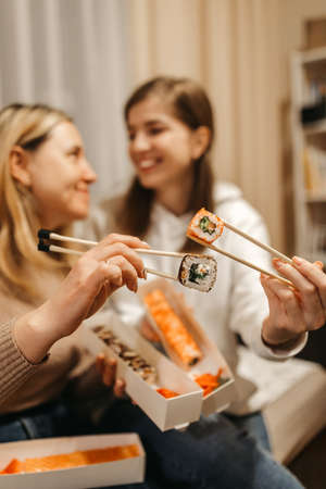Focus on rolls. Mom and daughter are holding sushi rolls with Chinese chopsticks. Blurred background. High quality photoの写真素材