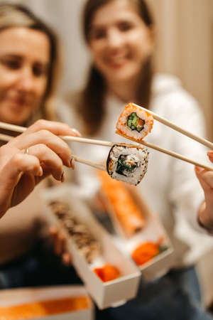 Focus on rolls. Mom and daughter are holding sushi rolls with Chinese chopsticks. Blurred background. High quality photoの写真素材