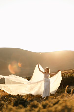 Beautiful bride in a white wedding dress stands posing in the sun and smiles in the mountains. High quality photoの写真素材