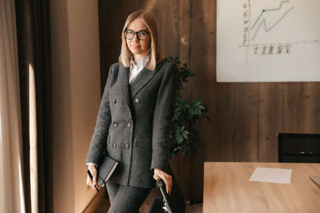 Businesswoman woman in her office stands with documents and a pen in her hands, office worker. A woman in a classic suitの写真素材