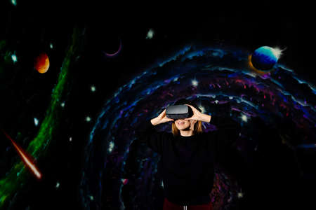 A young woman in virtual reality glasses reacts actively, is surprised, rejoices, against the background of space. High quality photoの写真素材
