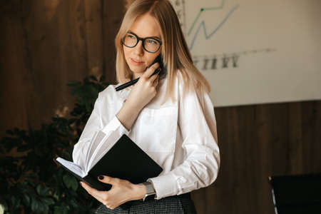 Business conversation on the phone in the office during working hours, a girl businesswoman is talking on a smartphone. High quality photoの写真素材