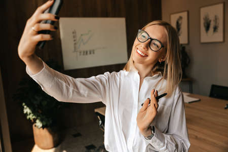 A beautiful happy blonde girl is broadcasting a live conversation through the phone, a conversation on a social network. High quality photoの写真素材