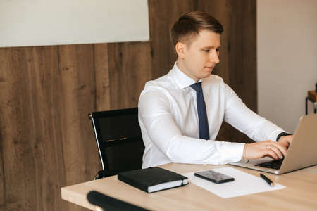 Young male businessman working on laptop in office.