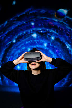 Happy girl uses virtual reality glasses on blue background of playroom. High quality photo