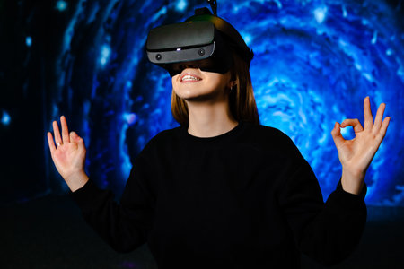 Happy girl uses virtual reality glasses on blue background of playroom. High quality photo