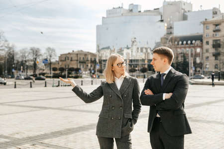 Businessman and businesswoman in office suits in the city. Girl holding a hand shows the city. Successful and confident office workers. High quality photoの写真素材