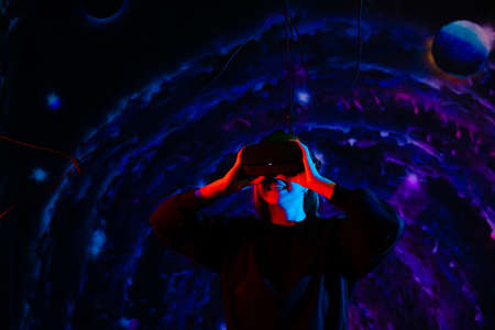 Young beautiful cheerful happy girl in virtual reality glasses with blue and red lights in the playroomの写真素材