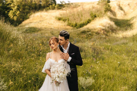 Beautiful newlyweds hugging in nature. Stylish couple together on the background of the hills.の写真素材