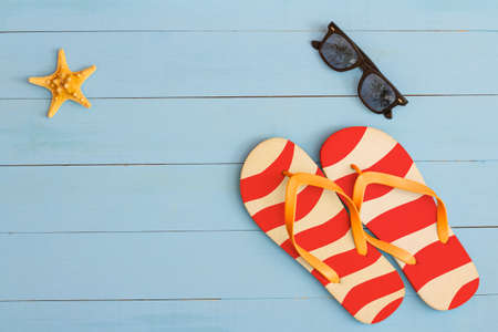 Summer time on a cool view on painted light blue wood table with sunglasses, flip flops and starfish