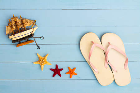 Summer time on a cool view on painted light blue wood table with sunglasses, flip flops, sailboat and starfishの写真素材